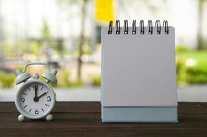 Alarm clock pointing at 2 o'clock with blank notepad on a bench. Copy space concept