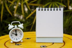 Alarm clock pointing at 10 o'clock with blank notepad. Blurred park background. Copy space concept photo