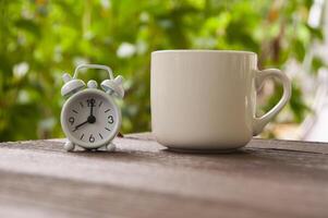 Alarm clock pointing at 8 o'clock with coffee cup on a bench. Copy space concept
