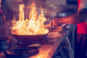 movimientos del chef mientras cocina en la cocina con fuego en la sartén