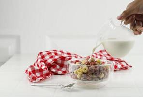 verter la leche en el recipiente con cereales coloridos froot loops. concepto de desayuno para niños, fondo blanco foto