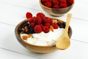 tazón de madera de crema batida de yogur griego con frambuesas y frutos secos foto