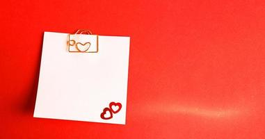 Square sheet for notes with a paper clip in shape of a letter and a heart. Decor of couples in love with hearts on a red background. Valentine's Day, message, greeting, declaration of love. Copy space photo