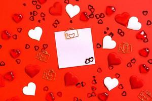 Square sheet for notes with a paper clip in shape of a letter and a heart. Decor of couples in love with hearts on a red background. Valentine's Day, message, greeting, declaration of love. Copy space photo