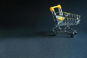 Empty grocery cart in the defocus from a supermarket on a black background. Black Friday, shopping cart, shopping, online store, sale, discounts. Space for text. Blurred photo
