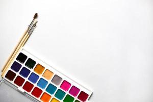 A palette of eighteen-color watercolors and paintbrushes on a white background with space for text. photo