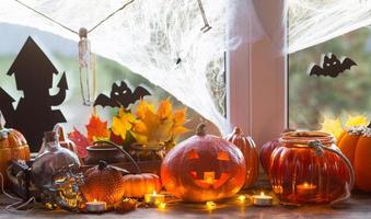 Festive decor of the house on the windowsill for Halloween - pumpkins, Jack o lanterns, skulls, bats, cobwebs, spiders, candles and a garland - a cozy and terrible mood photo