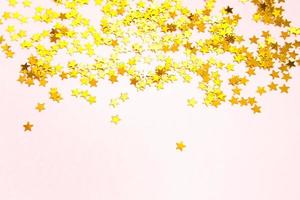 Gold sequins in the shape of stars shimmer on a pink background. Backgrounds with copyspace for a holiday, party decoration, Christmas and new year, birthday and anniversary. Gradient and texture photo