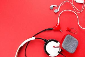 A heart-shaped headphone splitter for a couple in love. Connected to a red portable speaker and two pairs of headphones - flat lay. Valentine's day, love, modern technology, copy space photo