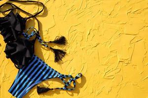 Blue with black stripes female swimsuit and sunglasses on a yellow background. The concept of a beach holiday, a trip to the sea, accessories for swimming, UV protection, tanning. Copyspace. Flatlay photo