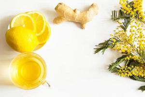 Herbal tea in a cup, ginger, lemon and acacia - strengthen immune system in the cold season. Allergies, fever, flu. Vitamin drink for health and ingredients on a white background. Copy space, flatly photo