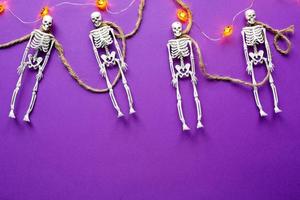 Halloween layout of garland of skeletons on a rope, glowing Jack o Lantern, pumpkins on a purple background. Flat lay horror and a terrible holiday photo