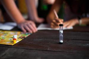 tablero de juego de mesa, fichas, cubo, temporizador en una mesa de madera oscura y manos en el fondo. el concepto de trabajo en equipo, relajación intelectual, evento corporativo, jugar en casa con niños. copie el espacio foto