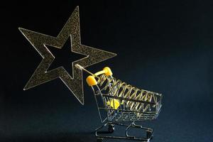 Shopping cart with a gold transparent star with sequins in the shape of a Christmas tree on a black background. Black Friday, buying gifts for the new year. Space for text photo