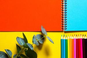 paleta arcoiris de lápices de colores con un cuaderno en espiral sobre un fondo amarillo, maqueta, puesta plana. regreso a la escuela, reclutamiento de estudiantes, artista, lecciones de dibujo. copie el espacio papelería para la creatividad