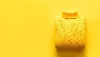 A yellow knitted sweater is rolled up on a yellow background, copyspace. Warm seasonal clothing for spring and autumn, lifting the mood photo