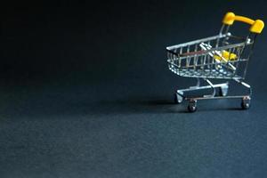 Empty grocery cart in the defocus from a supermarket on a black background. Black Friday, shopping cart, shopping, online store, sale, discounts. Space for text. Blurred photo