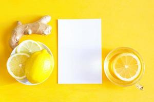 Medicinal tea in a cup, ginger, lemon-strengthen the immune system in the cold season and copy space, sheet for notes. Vitamin drink for health and ingredients on a yellow illuminating background. photo