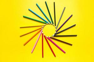 Set of colorful pencils on a yellow background is laid out in a circle in the shape of the sun. Copyspace, frame. Back to school, artist, drawing lessons. Stationery for creativity, draw photo