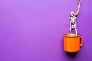 taza naranja sobre un fondo morado con terribles decoraciones de halloween. el concepto de la fiesta de halloween. bebida, diversión, fiesta. copie el espacio, maqueta, planamente foto