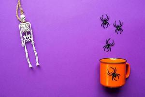 Orange mug on a purple background with terrible Halloween decorations. The concept of the Halloween holiday. Drink, fun, party. Copy space, mock up, flatly photo