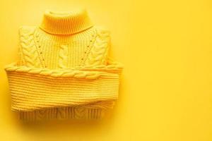 A yellow knitted sweater is rolled up on a yellow background, copyspace. Warm seasonal clothing for spring and autumn, lifting the mood photo