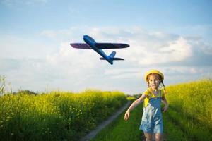 Girl in a yellow panama hat launches a toy plane into the field. Summer time, childhood, dreams and carelessness. Air tour from a travel agency on a trip, adventure and vacation. Village, cottage core photo