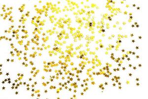 Gold sequins in the shape of stars shimmer on a white background. Backgrounds with copyspace for a holiday, party decoration, Christmas and new year, birthday and anniversary. Gradient and texture photo