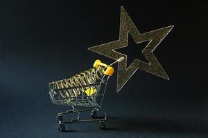 Shopping cart with a gold transparent star with sequins in the shape of a Christmas tree on a black background. Black Friday, buying gifts for the new year. Space for text photo