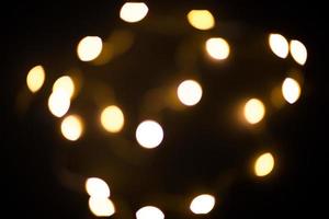 Yellow and gold lights garland in a blur on a black background. Bokeh of flying circles in the defocus. Festive atmosphere of Christmas and new year. Celebrate background photo