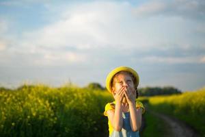 Girl in yellow blooming field covered her nose and face with hands and wrinkled up - an unpleasant smell, irritation, allergy. Allergic reaction to flowering in spring and summer, mosquito repellent photo