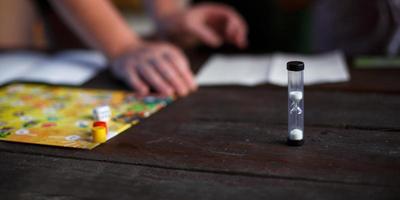 Board game board, chips, cube, timer on a dark wooden table and hands in the background. The concept of teamwork, intellectual relaxation, corporate event, playing at home with children. Copy space