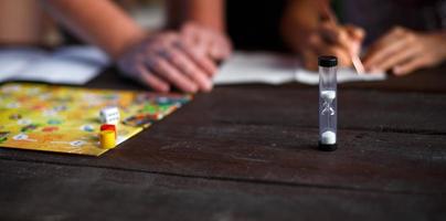 tablero de juego de mesa, fichas, cubo, temporizador en una mesa de madera oscura y manos en el fondo. el concepto de trabajo en equipo, relajación intelectual, evento corporativo, jugar en casa con niños. copie el espacio foto