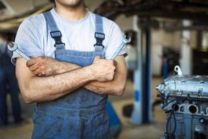 The hand of a car repairman with keys and a special tool on the background of the service area. A mechanic in a car service station in uniform. Copy space photo