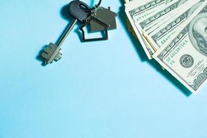 Home key with a keychain on a stack of 100 bills on a blue background. Purchase of an apartment, house, real estate, business, mortgage and housing loan from bank, savings, cash, moving. Copy space photo