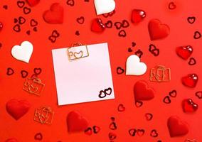 Square sheet for notes with a paper clip in shape of a letter and a heart. Decor of couples in love with hearts on a red background. Valentine's Day, message, greeting, declaration of love. Copy space photo