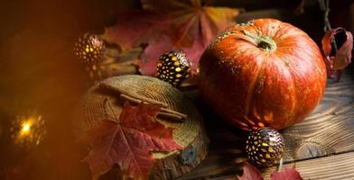 Orange natural round pumpkin on a wooden table with fallen yellow and red maple leaves, cinnamon sticks. Lights garlands, warm autumn atmosphere, thanksgiving, harvest festival, Halloween. Copy space photo