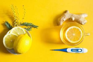 Medicinal tea in a cup, ginger, lemon, acacia-strengthen the immune system in cold season, thermometer and copy space, sheet for notes. Vitamin drink for health and ingredients on yellow background. photo