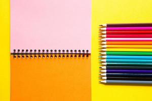 Rainbow palette of colored pencils with a spiral notebook on a yellow background,mock up, flat lay. Back to school, student recruitment, artist, drawing lessons. Copy space. Stationery for creativity photo