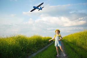 Girl in a yellow panama hat launches a toy plane into the field. Summer time, childhood, dreams and carelessness. Air tour from a travel agency on a trip, adventure and vacation. Village, cottage core photo
