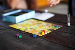 tablero de juego de mesa, fichas, cubo, temporizador en una mesa de madera oscura y manos en el fondo. el concepto de trabajo en equipo, relajación intelectual, evento corporativo, jugar en casa con niños. copie el espacio foto