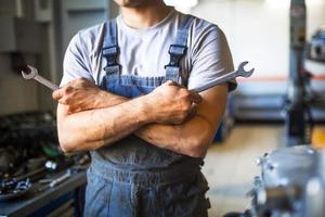 The hand of a car repairman with keys and a special tool on the background of the service area. A mechanic in a car service station in uniform. Copy space photo