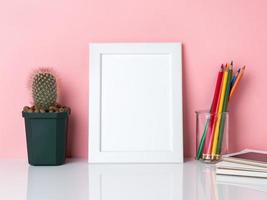 marco blanco en blanco, crayón en frasco, plantar cactus en una mesa blanca contra la pared rosa con espacio para copiar foto