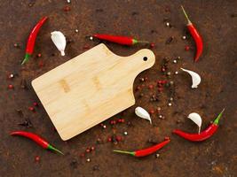 red hot chili pepper pods and peas, cutting board, garlic clove on dark rusty metal background, top view, copy space photo