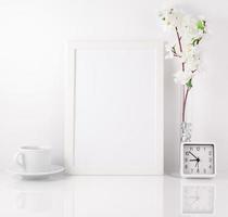 White frame, flower in vase, cup with tea or coffee, clock on wh photo