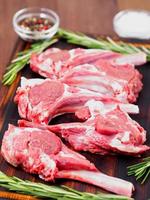 Raw lamb cutlets on bone on dark brown wooden background, lamb ribs, side view, vertical photo