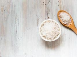 White bowl with large sea salt and wooden spoon on white wooden table. photo