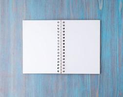 Open notebook on spring with white paper for notes and drawing. Light background, blue wood, top view. photo