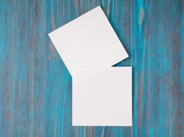 two white piece of paper for notes, square shape for record reminders on a blue wooden table, top view photo