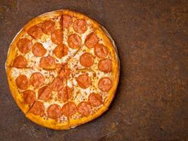 round Italian pizza pepperoni on a rusty metal desk top view, empty space for text. photo